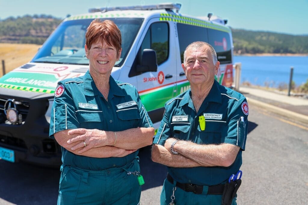 Two Volunteer Ambulance Officers smiling and standing in front of an ambulance. A dam is in the background.