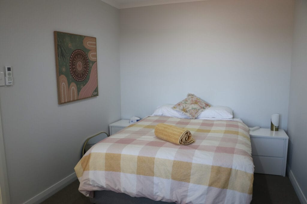 A clean, smart-looking bedroom featuring a double bed with brightly coloured bedding and artwork on the walls.