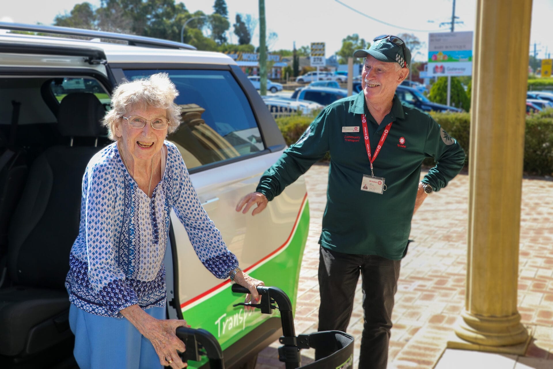 A man in a St John WA Community Transport Uniform holds a van door open for a woman with a walking frame