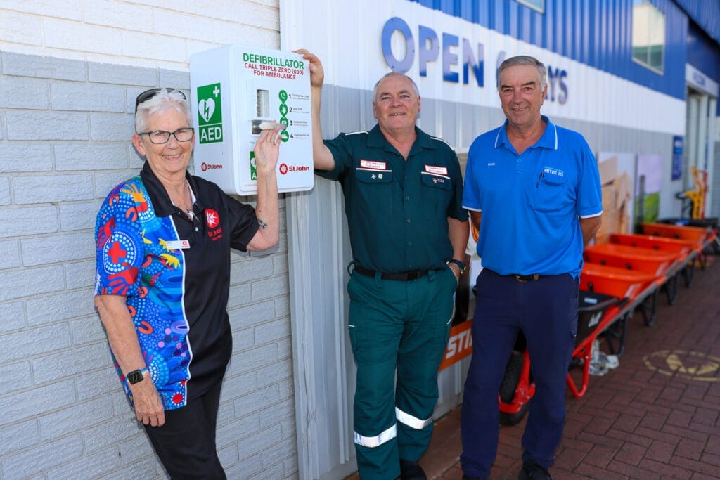 Three people stand next to an Automated External Defibrillator (AED) outside a hardware store.