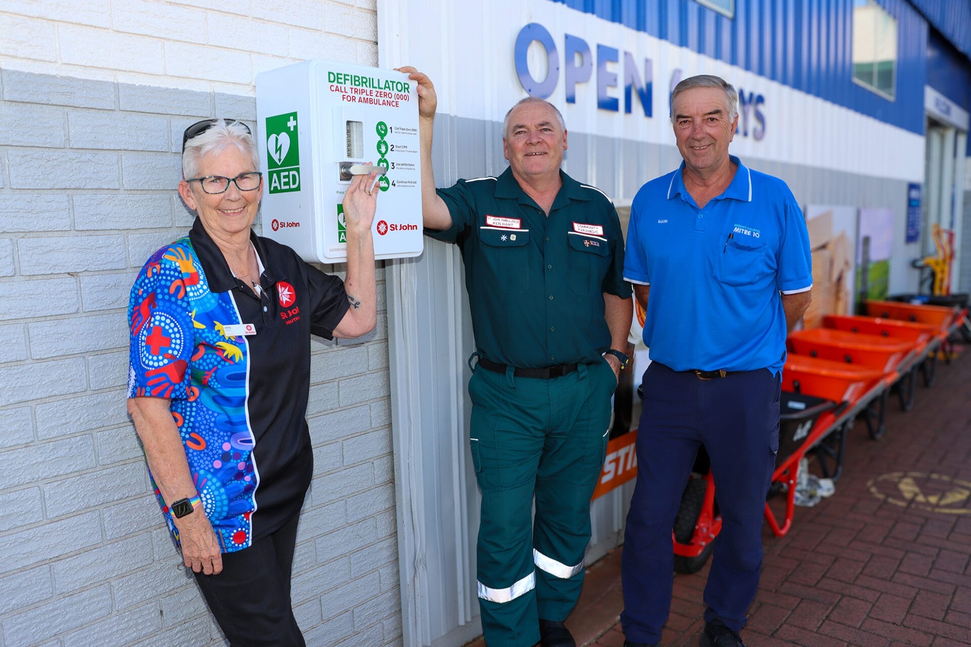 Three people stand next to an Automated External Defibrillator (AED) outside a hardware store.