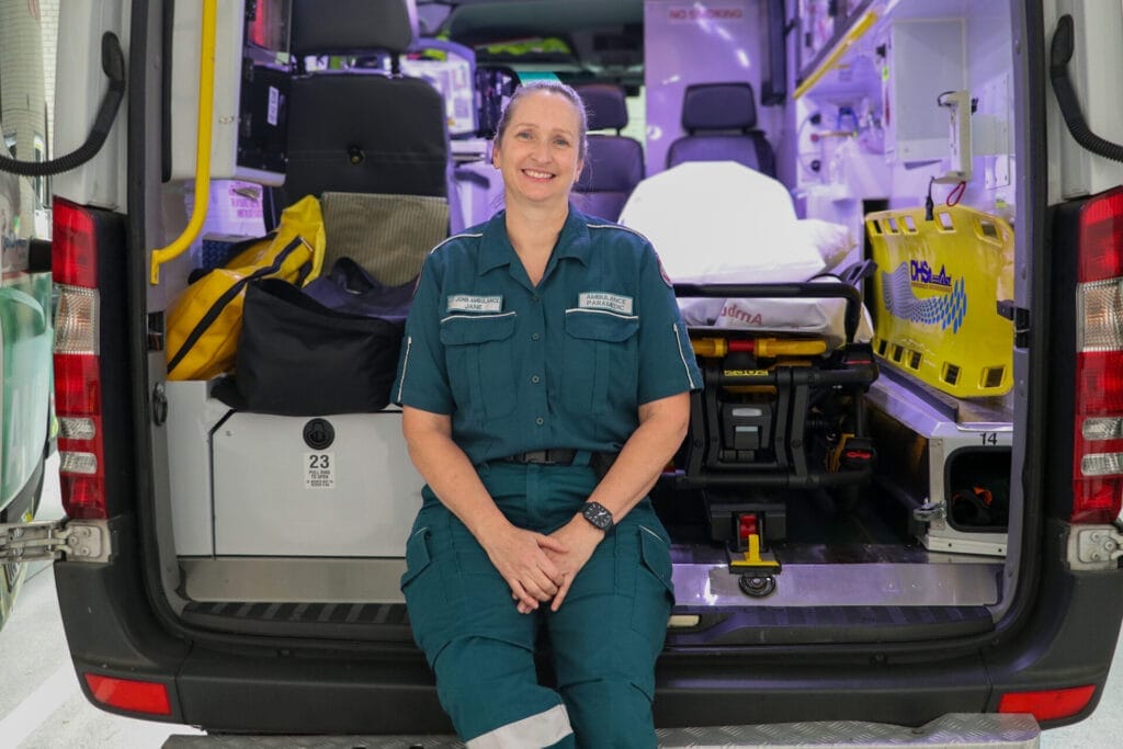 A woman in a green uniform sits in the back of an ambulance