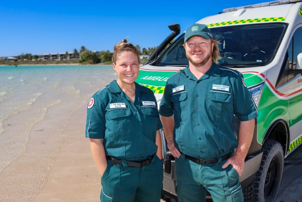 Two people in uniforms standing in front of an ambulance on a tropical beach.